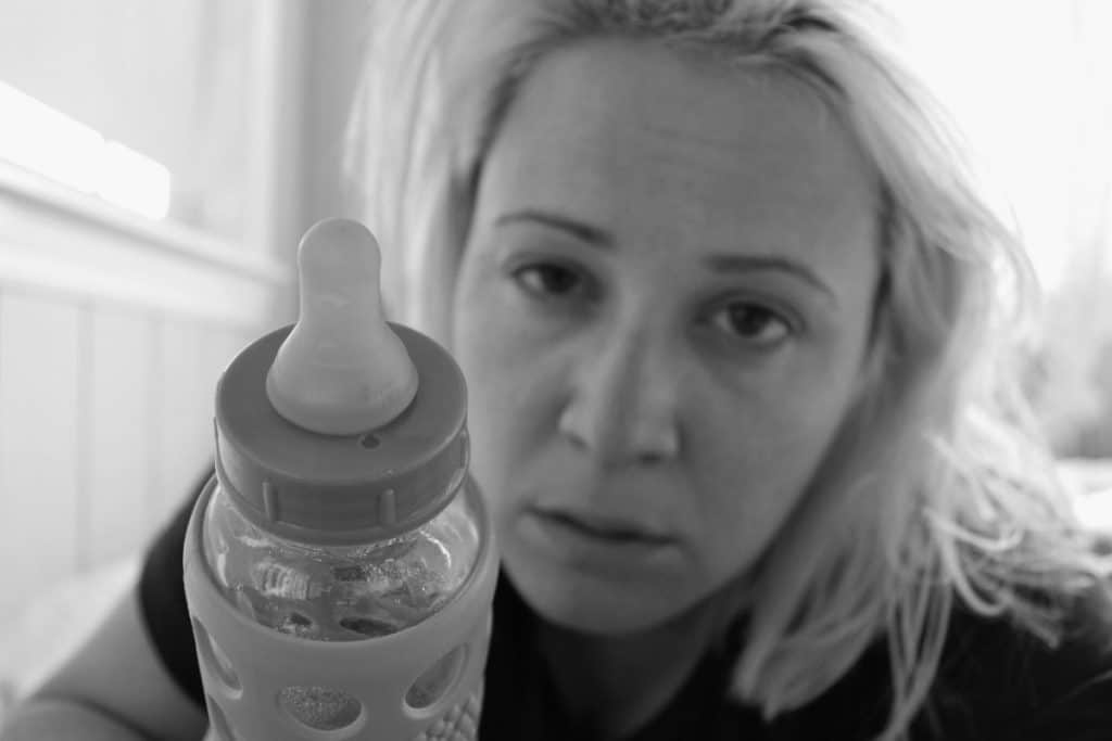 Maman à 40 ans fatiguée tendant un biberon à son bébé