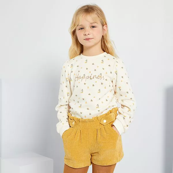 Fillette habillée d'un polo manches longues et d'un short de la marque Kiabi